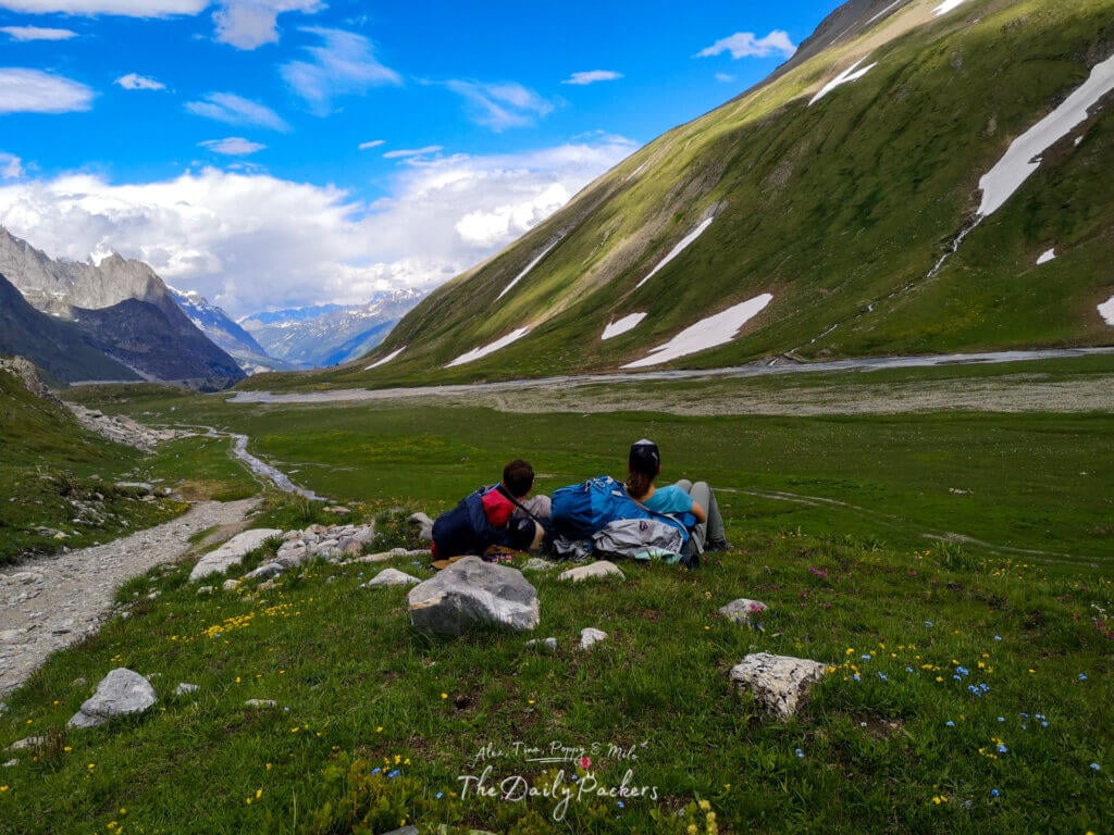 Deux randonneurs se reposant sur l'herbe avec des sacs à dos, profitant de larges vues sur une vallée verte.