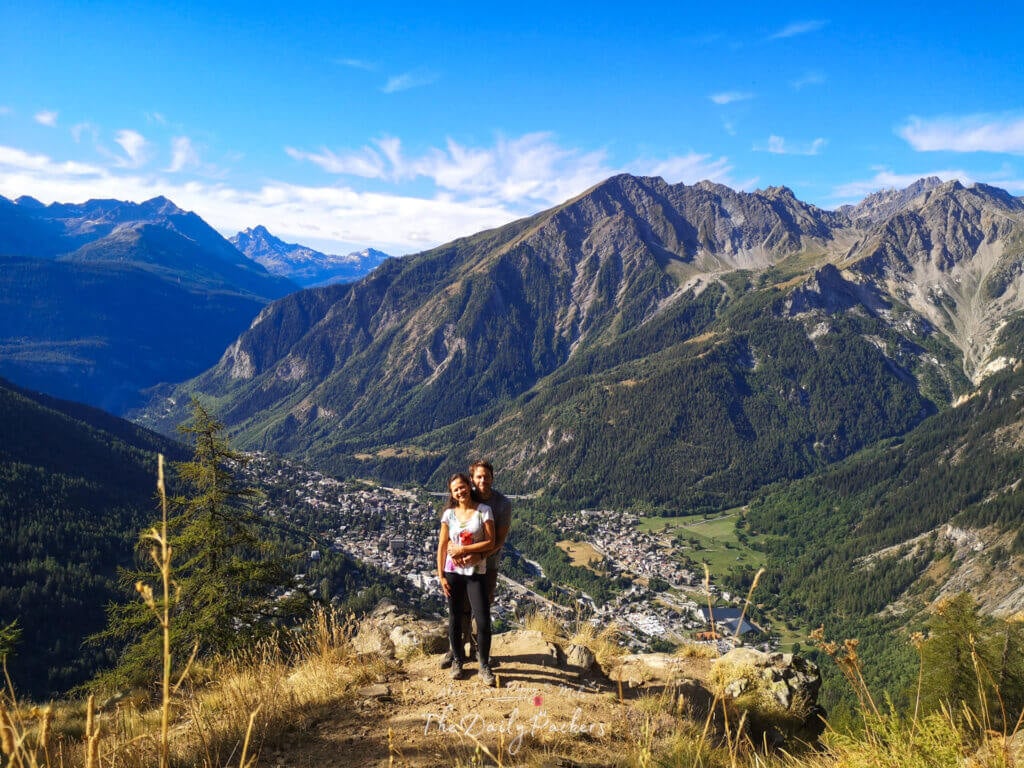 Couple posing on a mountain viewpoint overlooking Courmayeur and the surrounding alpine peaks.