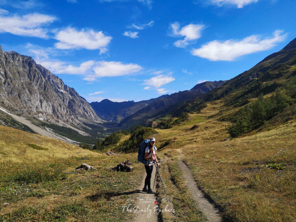 Backpacker standing on a mountain path with a wide valley opening into the distance.