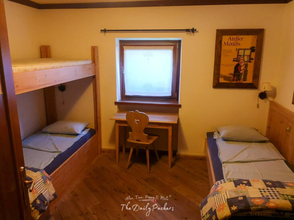 Simple dormitory room at Rifugio Bonatti with wooden bunk beds, a single bed, and a small desk by the window.