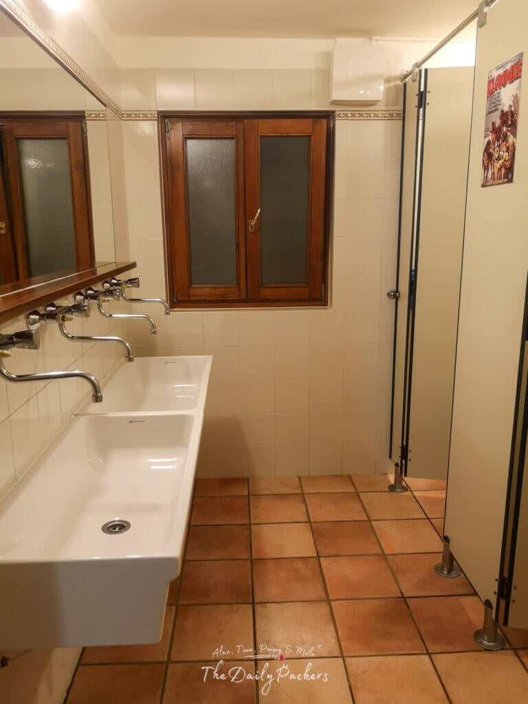 Shared bathroom at Rifugio Bonatti with tiled floors, sinks, mirrors, and individual shower cabins.