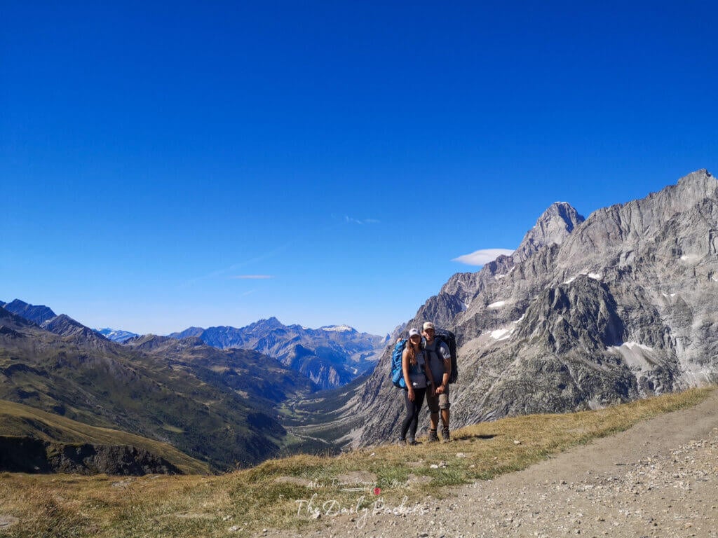 Couple standing on a trail with stunning alpine peaks and valleys around Grand Col Ferret.