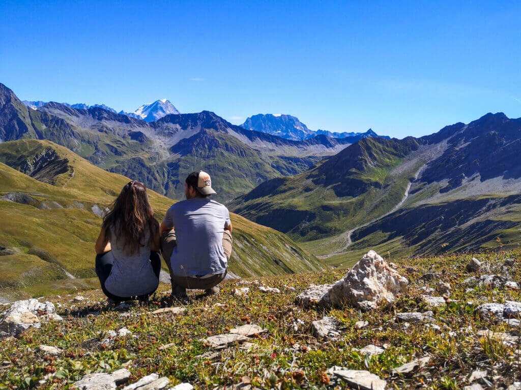 Couple sitting on grassy slope admiring the valley view near La Fouly and thinking on how to Escape the TMB