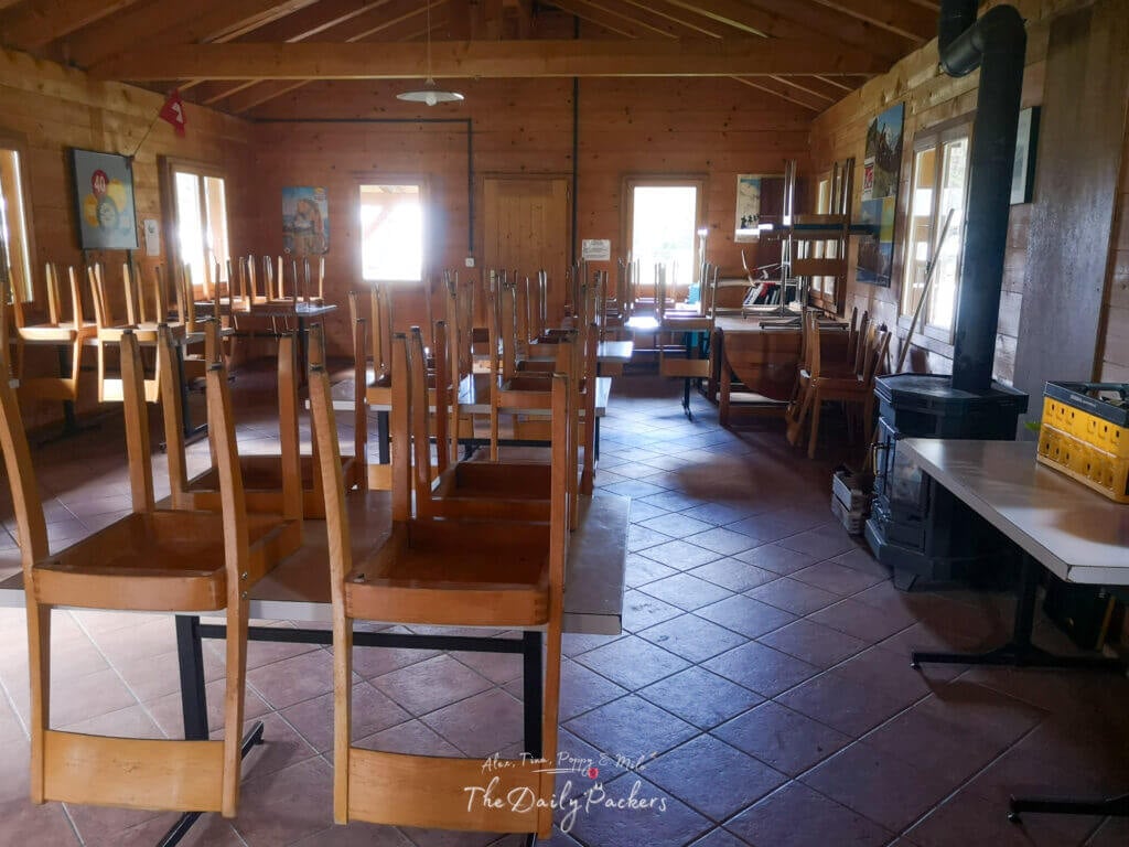 Dining room with wooden chairs stacked on tables inside Camping des Glaciers.