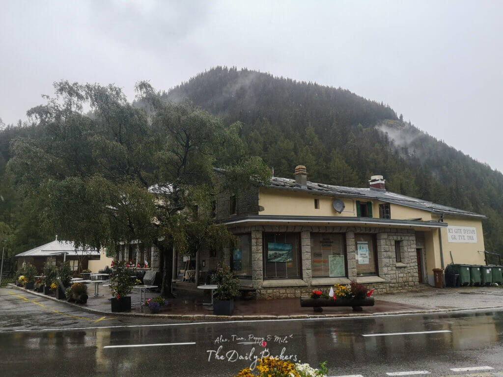 Mountain hut and road at Col de la Forclaz on a rainy day surrounded by misty forest slopes.