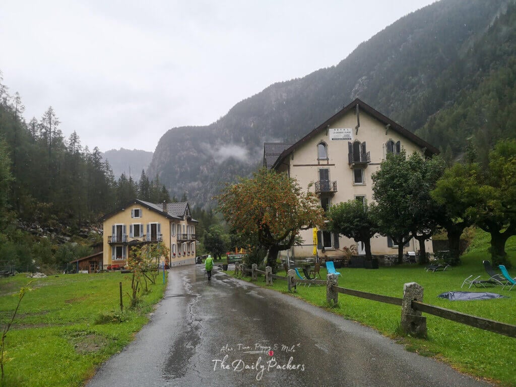Charming yellow hotel at Trient with hiker arriving on a rainy day, surrounded by mountains.