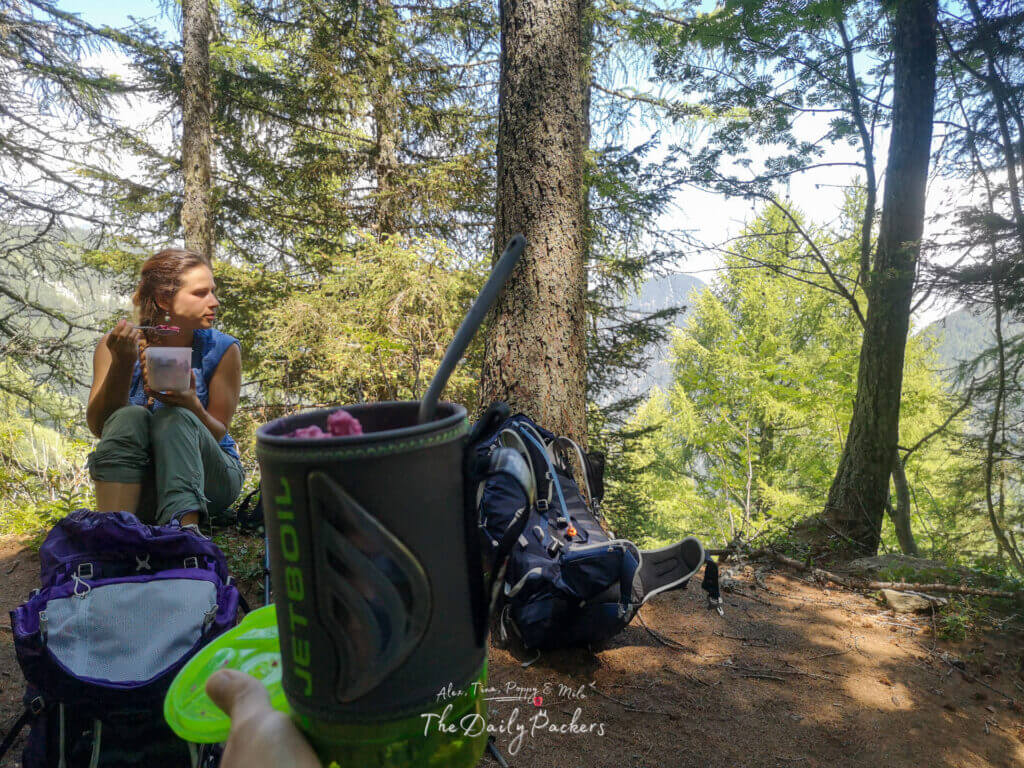 Trail lunch in the woods: Jetboil mug in foreground, hiker eating beside packs.