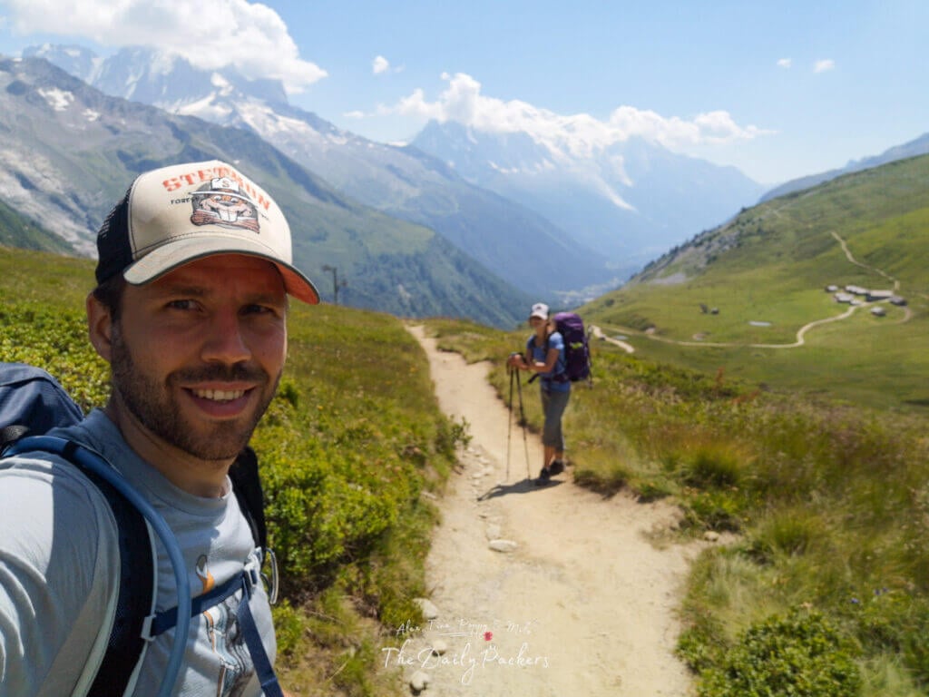 Couple hiking a ridgeline path; selfie with Mont Blanc in the distance.