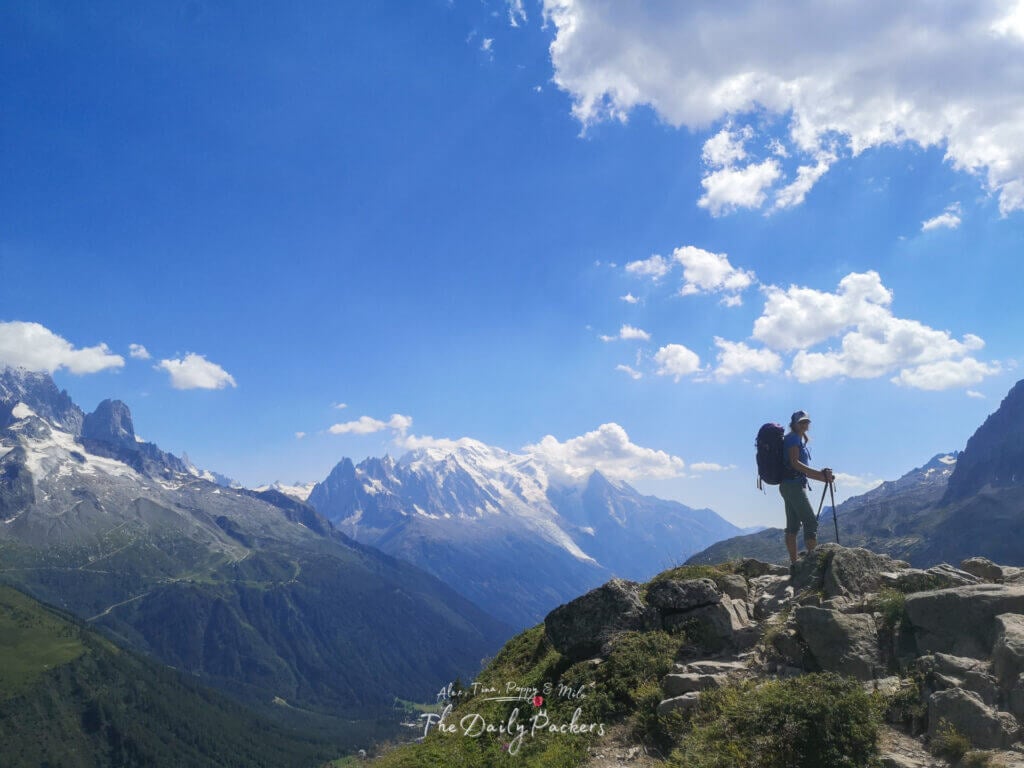 Hiker standing on a rocky outcrop with trekking poles, overlooking Mont Blanc and the French Alps.