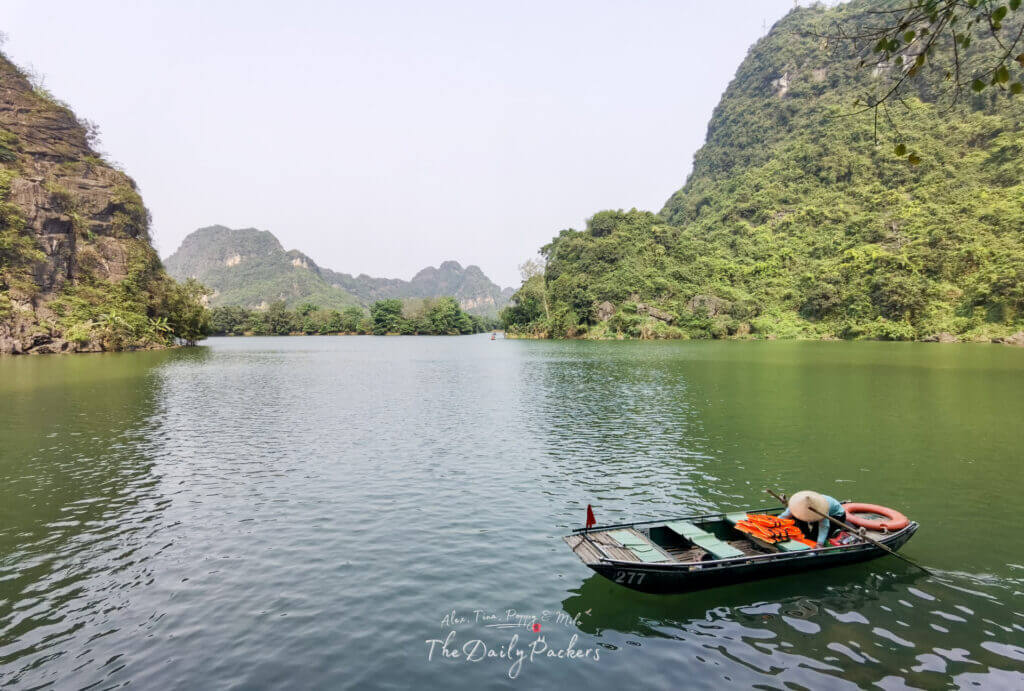 A single rowing boat floating on Trang An’s emerald waters with limestone peaks in the background.