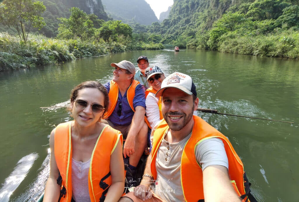 Tourists wearing orange life jackets enjoying a Trang An boat tour surrounded by stunning karst scenery.