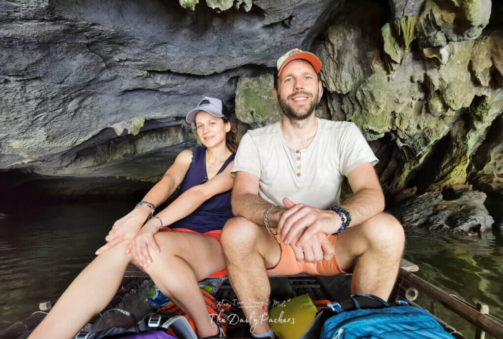 Travelers smiling inside a cave boat tour at Van Long Nature Reserve with rocky walls in the background.