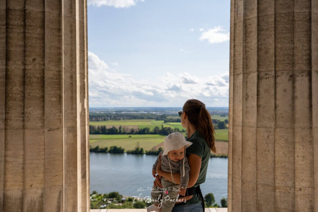 Femme tenant un bébé debout entre les hautes colonnes du mémorial du Walhalla surplombant le Danube.