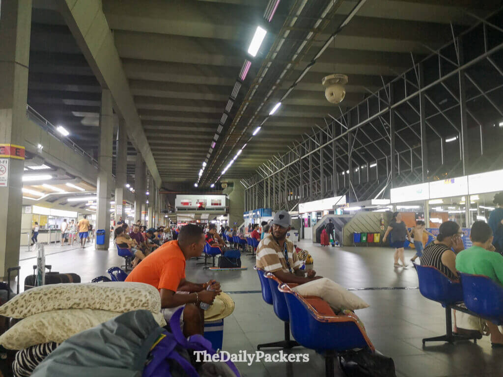 Interior of the main bus terminal in Florianópolis, Brazil, with travelers waiting for their buses under the large concrete ceiling.