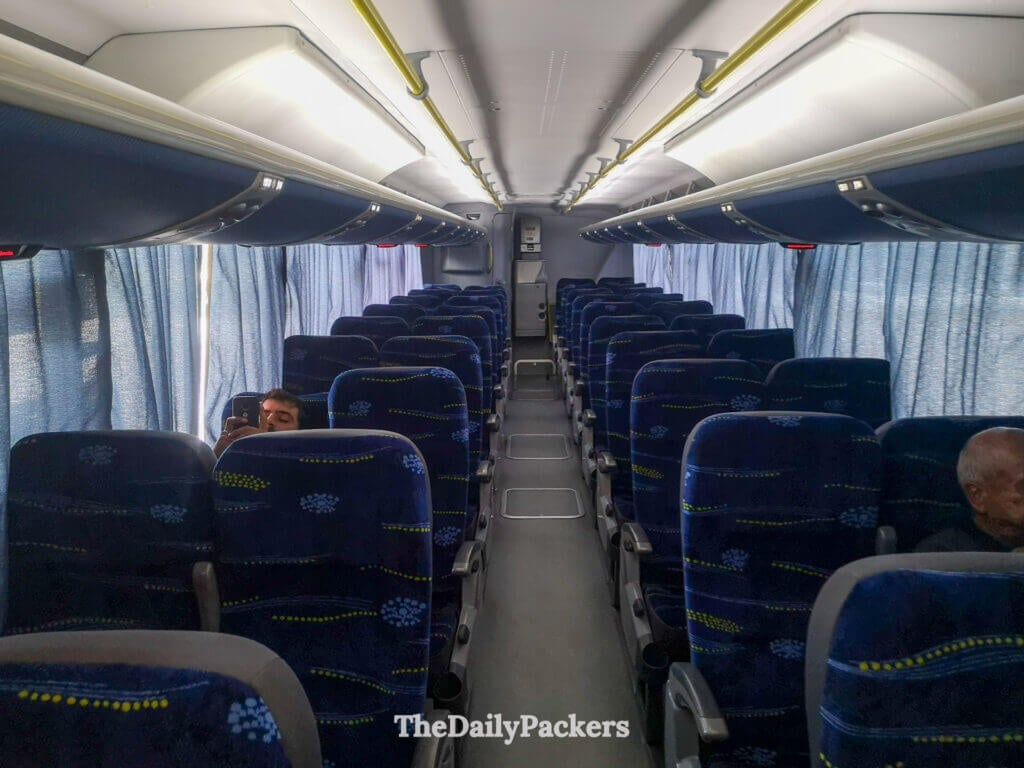 Inside view of the Embaixador bus to Chuy, showing rows of blue seats and passengers settling in.