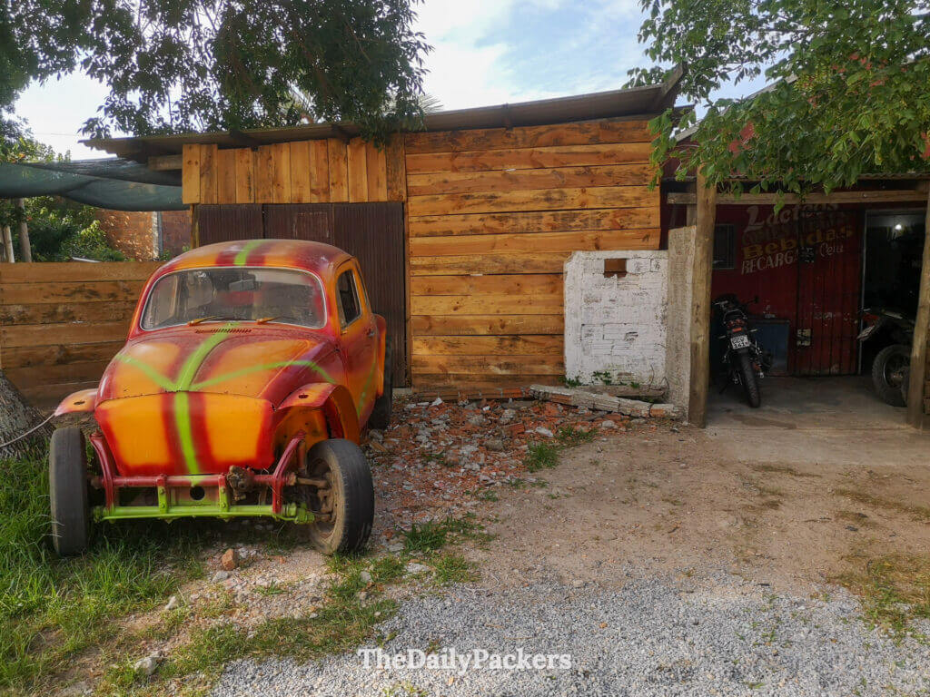 Colorful vintage car painted in red, yellow, and green parked outside a wooden shed in Chuy.