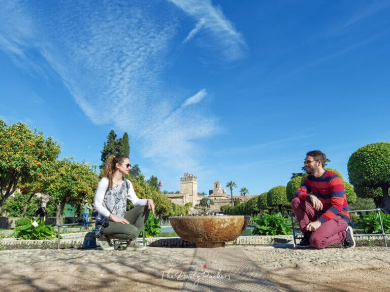 Couple enjoying a sunny day at the Alcázar de los Reyes Cristianos gardens in Córdoba, surrounded by orange trees and fountains.