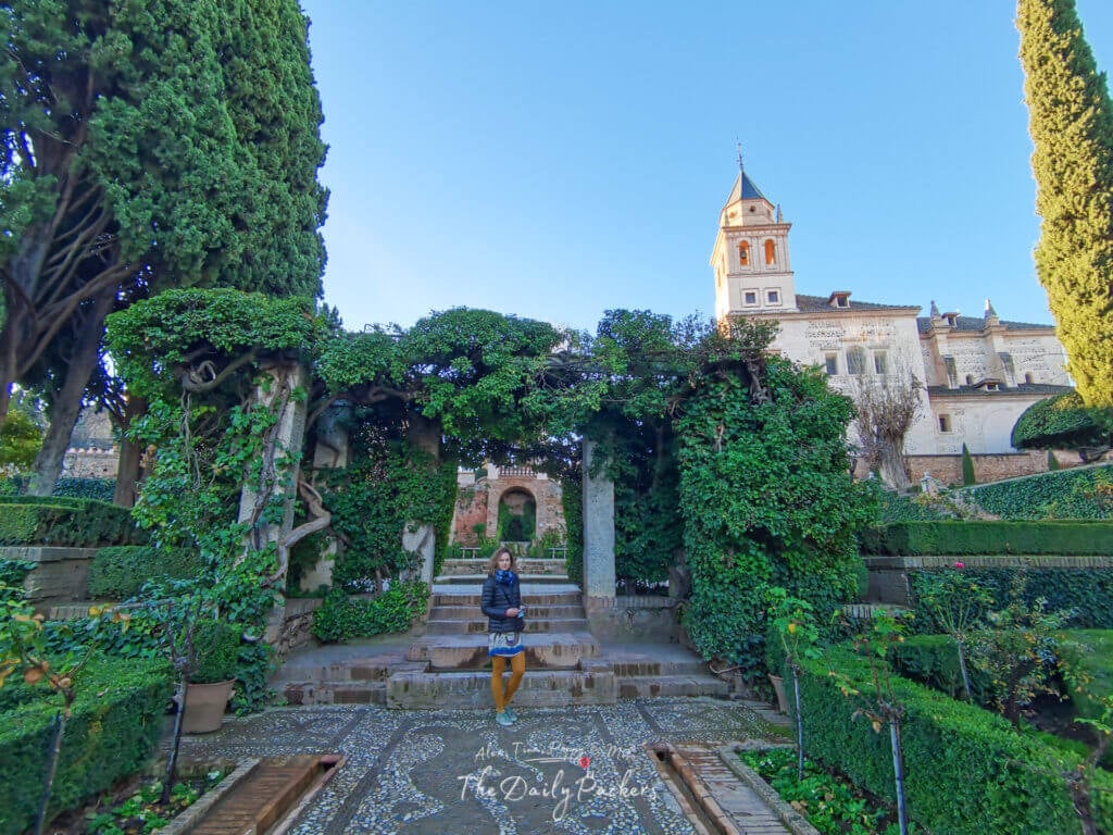 Femme dans les jardins de l'Alhambra à Grenade, entourée d'une végétation luxuriante et de bâtiments historiques en arrière-plan