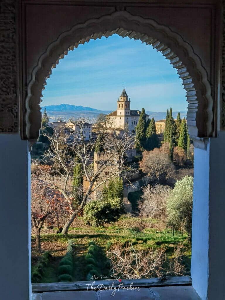 Vue de l'Alhambra à Grenade encadrée par un arc mauresque, surplombant les jardins luxuriants et les montagnes lointaines.