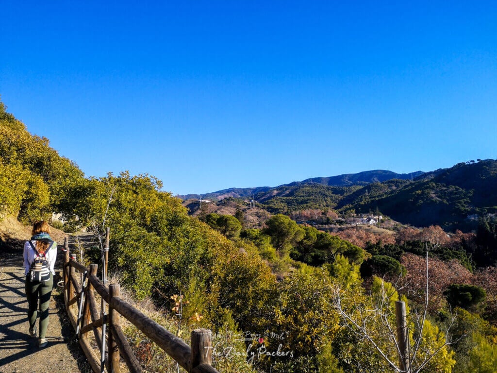 Traveler walking along a mountain trail near Málaga with panoramic views of the surrounding hills and greenery.