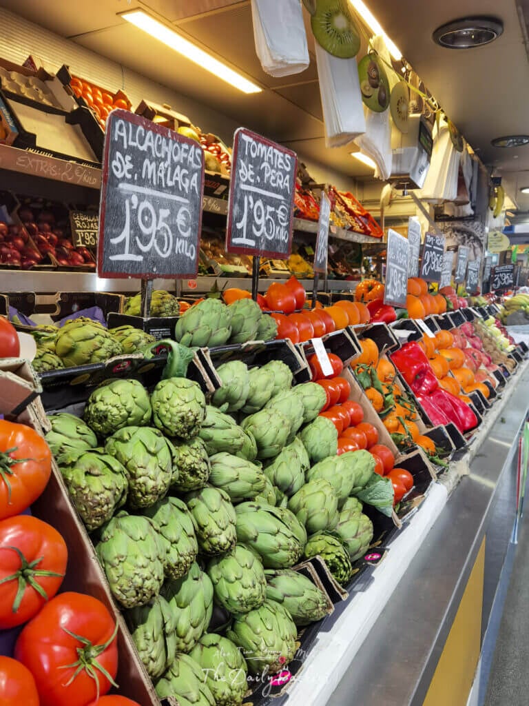 Colorful vegetable stall at Mercado Central de Atarazanas featuring fresh artichokes, tomatoes, and local produce from Málaga.