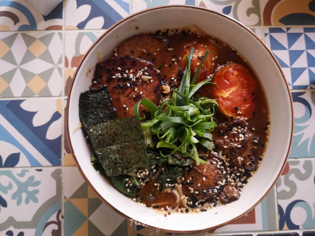 Plat végétalien avec tempeh grillé, brocoli, champignons et une fleur comestible servi au MIMO Vegan Bistrot à Málaga, Espagne.
