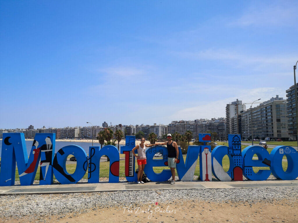 Voyageurs posant devant le panneau coloré de Montevideo avec la plage de Pocitos et la ligne d'horizon de la ville en arrière-plan.