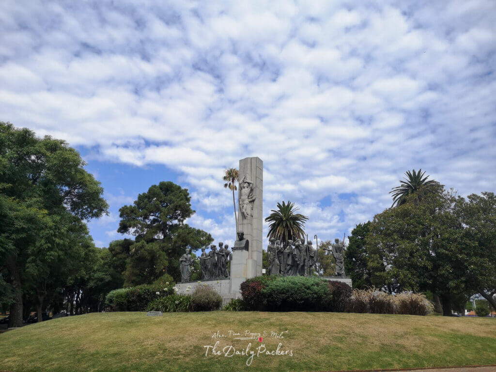 Monument surrounded by palm trees and greenery in Parque Rodó, Montevideo, under a sky filled with soft clouds.