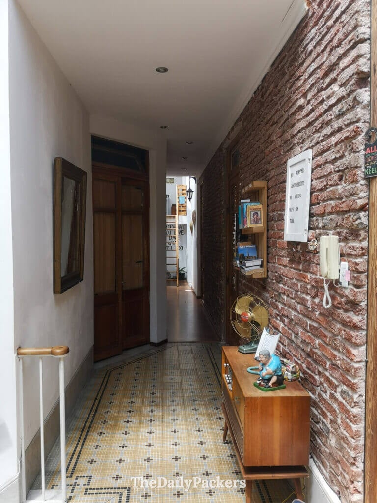 Couloir rustique avec des murs en brique, des meubles vintage et un sol carrelé menant aux chambres d'hôtes.