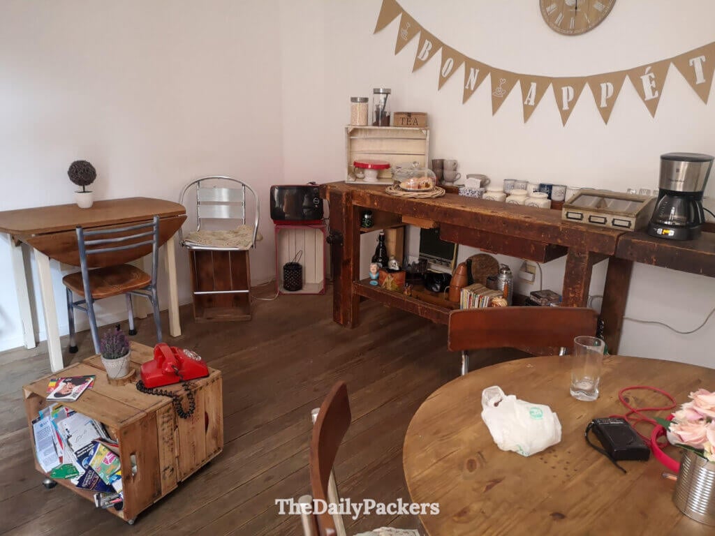 Espace commun chaleureux et accueillant avec des tables en bois, un coin café et une bannière "Bon Appétit".