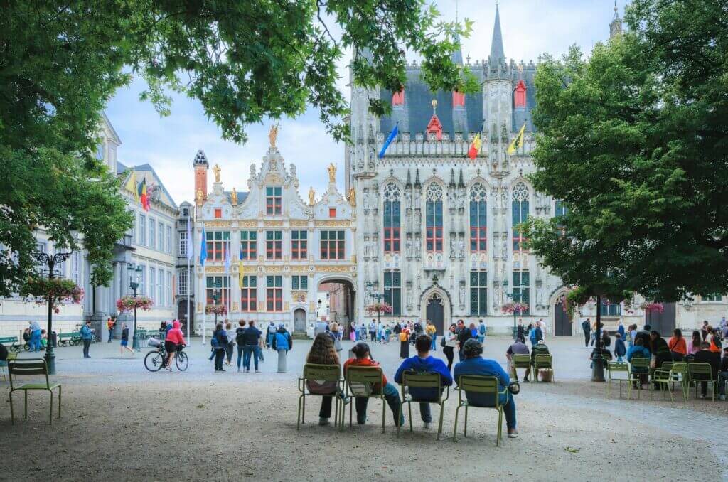 Des personnes profitant d'une journée d'été à l'Hôtel de Ville de Bruges, mettant en valeur la belle architecture flamande.