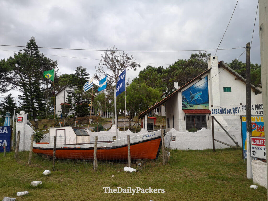 White seaside cottages in Punta del Diablo with maritime murals, flags, and a decorative fishing boat in front.