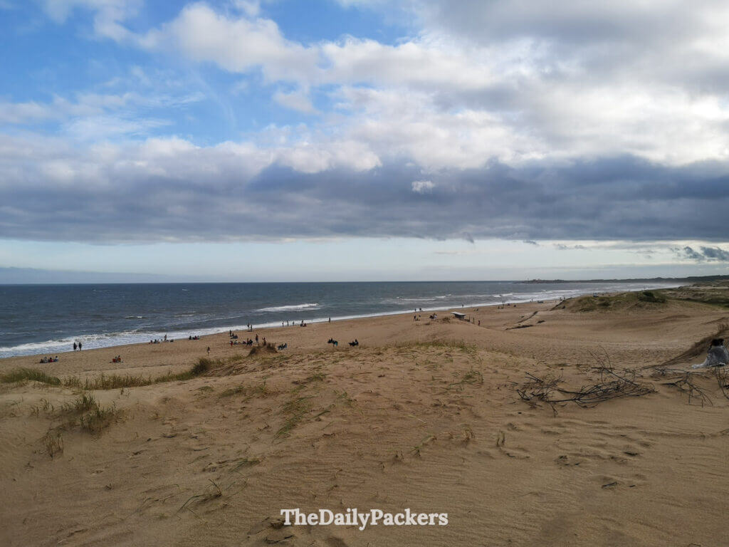 View of Playa de la Viuda, one of Punta del Diablo’s main beaches, surrounded by sand dunes and people relaxing by the sea.