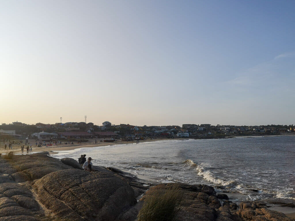 Golden hour view of Playa del Rivero, with people relaxing on the rocks and walking along the beach at sunset.