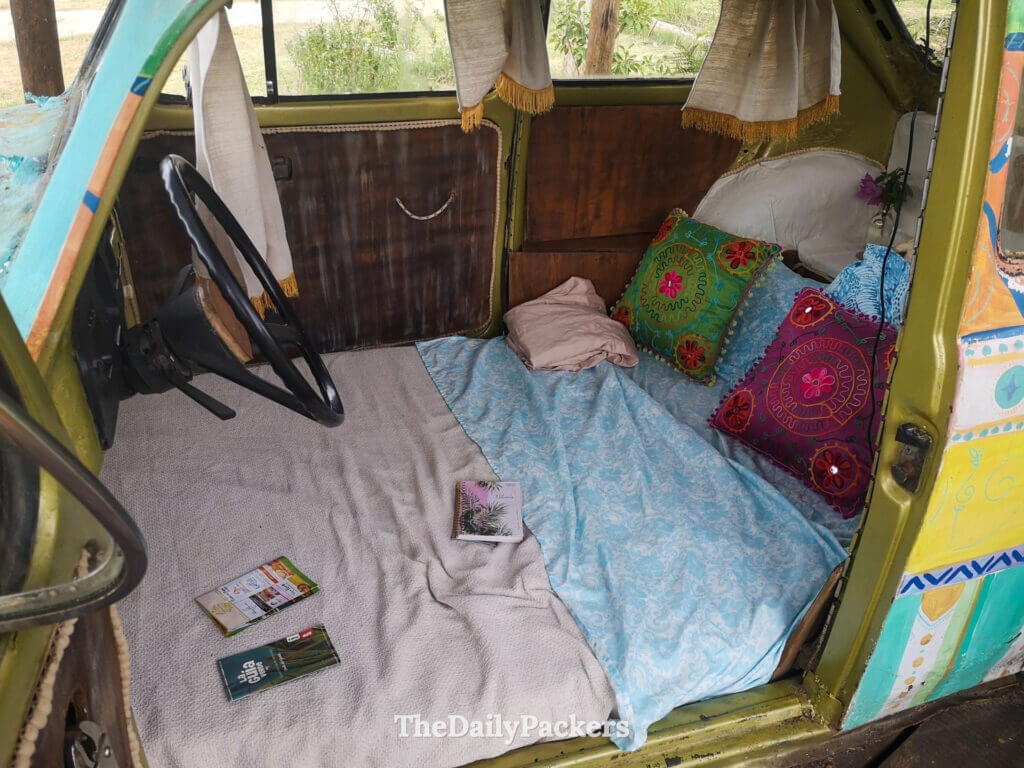 Intérieur d'une Coccinelle VW convertie en espace de couchage douillet, décorée de coussins et de couvertures aux motifs vifs.