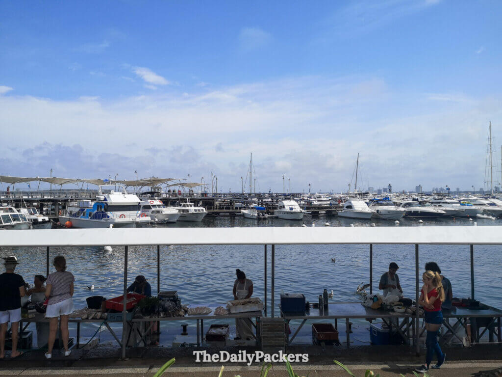 Marché aux poissons local près du port où les vendeurs proposent des fruits de mer frais à côté des bateaux sur le front de mer calme.