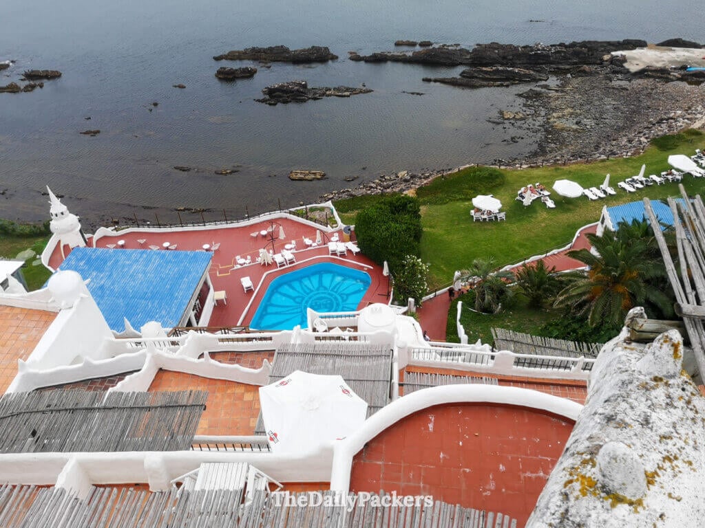 Aerial-style view of Casa Pueblo showing the pool, red terraces, and gardens by the ocean.