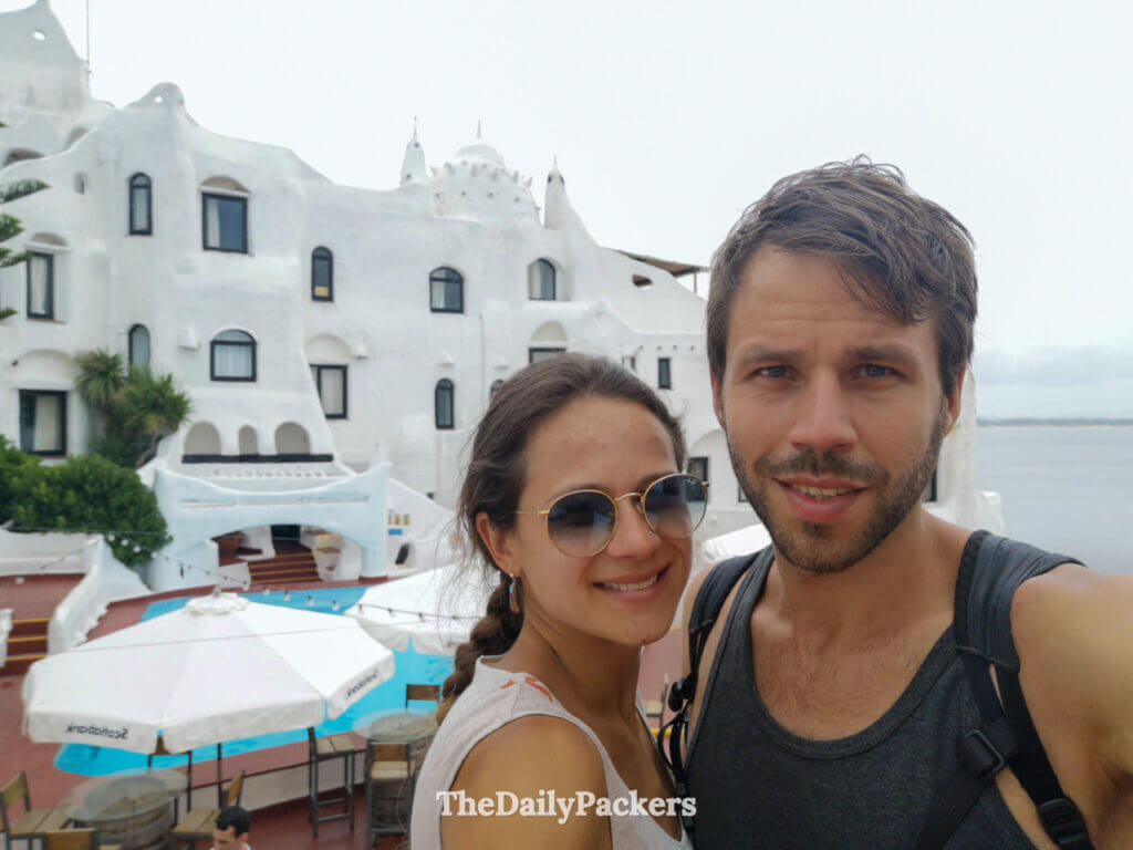 Couple smiling in front of Casa Pueblo’s whitewashed walls and pool overlooking the ocean in Punta Ballena.