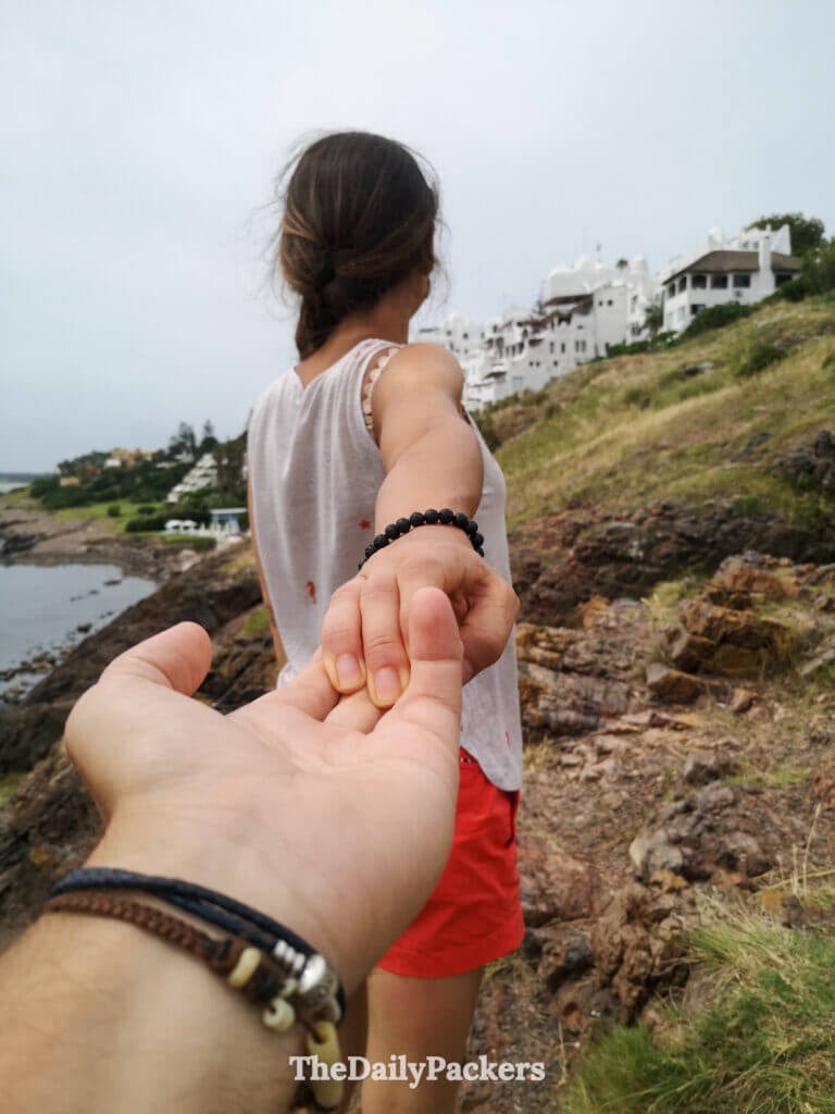 Romantic travel shot of a couple holding hands while walking toward Casa Pueblo on Punta Ballena’s rugged coast.