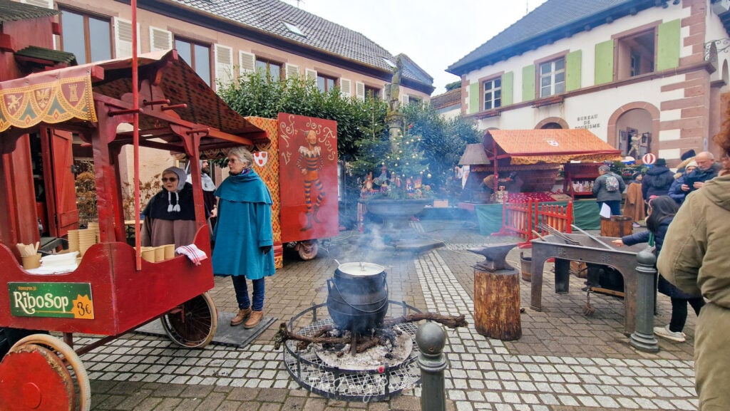 Étals à thème médiéval et vendeurs costumés au marché de Noël de Ribeauvillé près de la Fontaine du Vigneron.