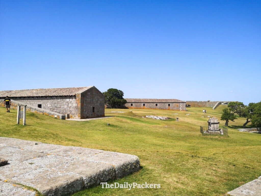 View of the Santa Teresa Fortress grounds with stone buildings and grassy courtyards beneath a clear sky.