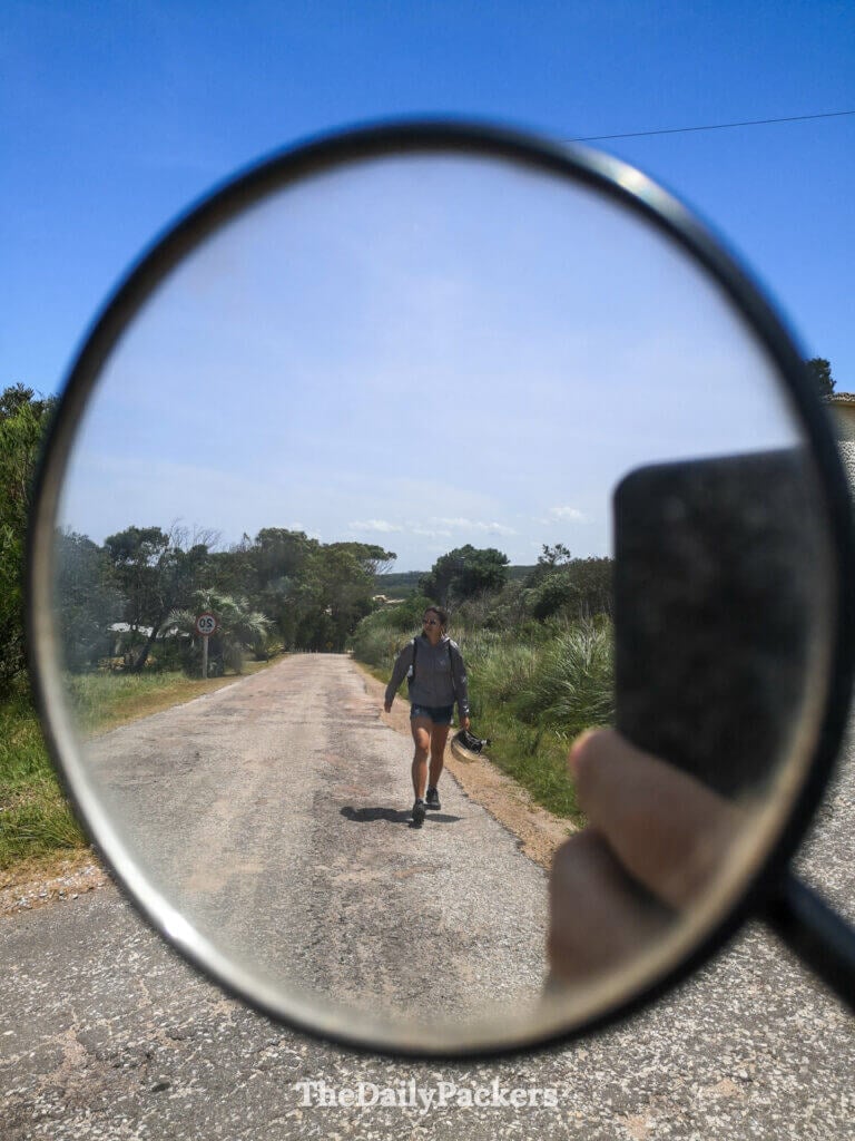 Creative shot showing a woman walking on a quiet park road, reflected in a motorcycle mirror.