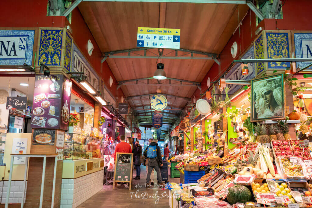 Couloir animé à l'intérieur du Mercado de Triana à Séville, bordé d'étals espagnols traditionnels vendant des pâtisseries, de la viande et des produits.