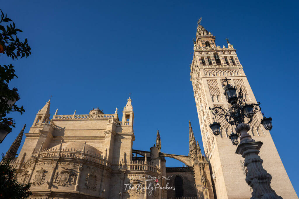 Gros plan de la cathédrale de Séville et de la tour de la Giralda sous un ciel bleu clair, mettant en valeur la splendeur gothique de la ville.