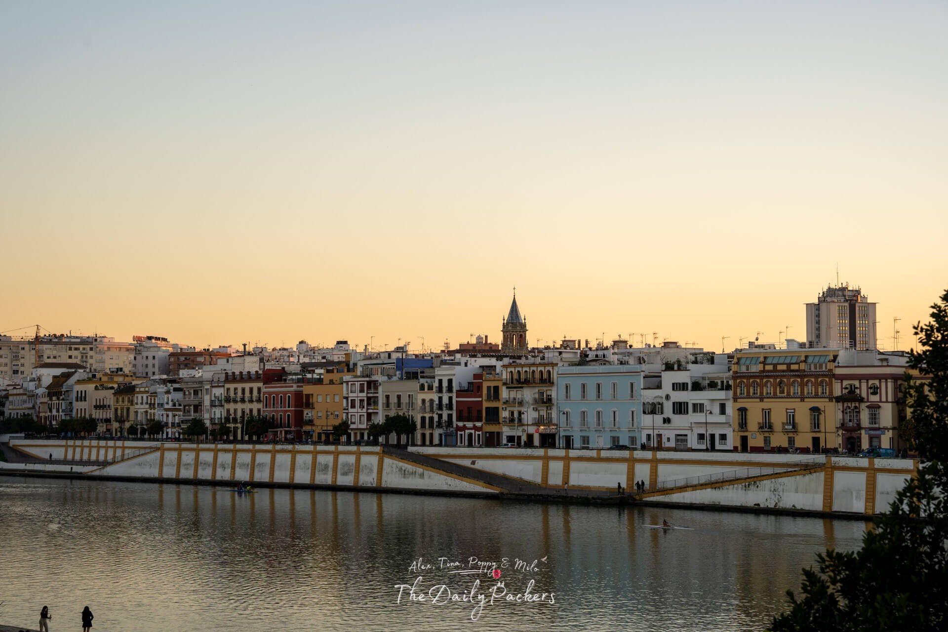 Golden sunset over Seville’s Triana district, reflecting colorful buildings on the calm waters of the Guadalquivir River.