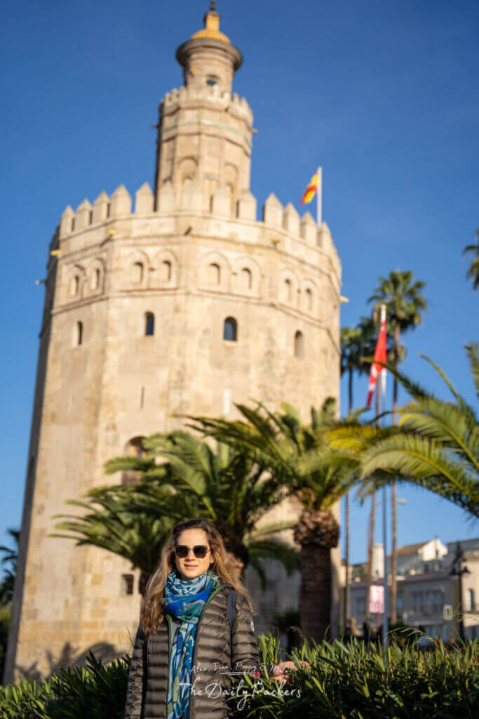 Voyageur posant devant la Torre del Oro de Séville, entourée de palmiers et baignée de soleil doré.