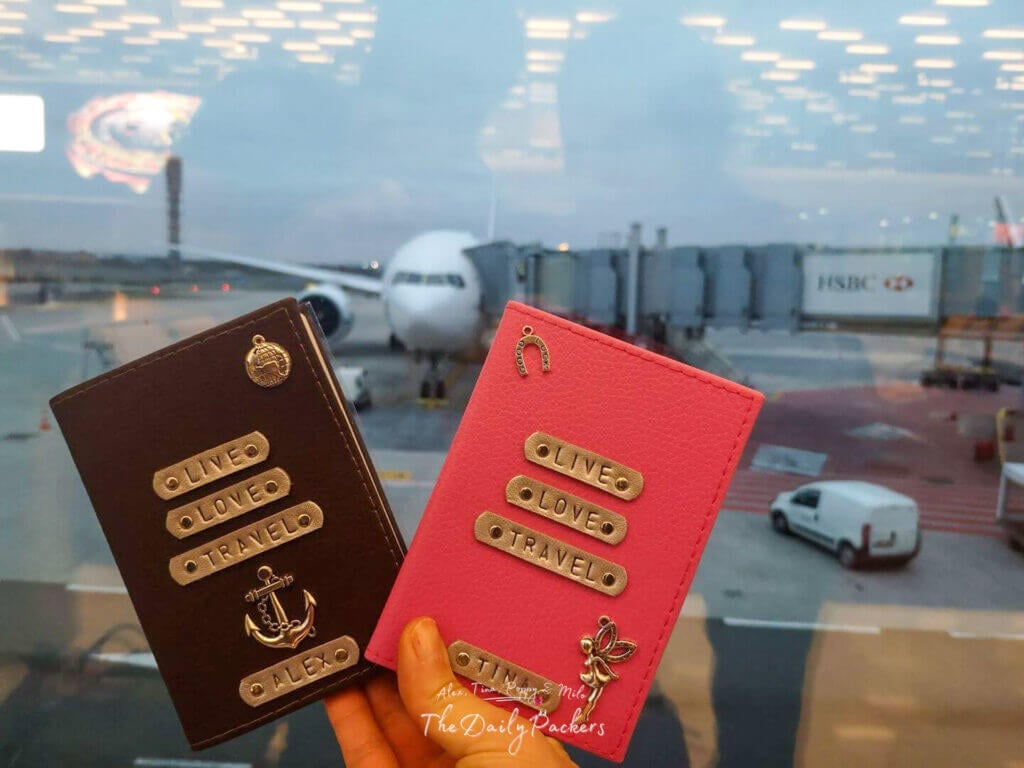 Close-up of two travel passport covers with “Live Love Travel” designs held up in front of an airplane at the gate and ready for all travel visa requirement