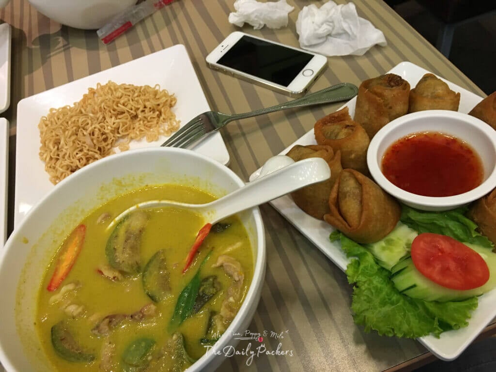 Table with Thai curry, spring rolls, and noodles served with dipping sauce in a restaurant.