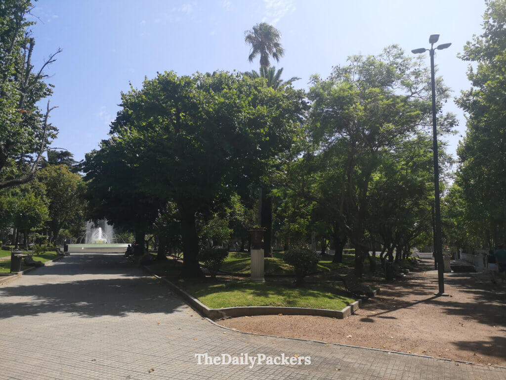 Scène matinale paisible sur la Plaza 25 de Agosto, un parc verdoyant de Colonia del Sacramento avec une fontaine centrale et des bancs ombragés.