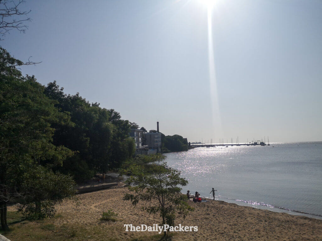 Petite plage de sable le long de la Rambla à Colonia del Sacramento, avec des arbres et des vagues fluviales calmes sous le soleil de l’après-midi.
